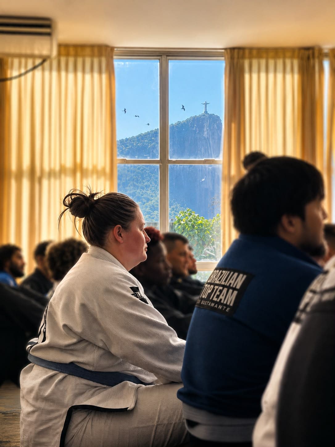 Martial artists in gis sit before a window overlooking Rio's Christ the Redeemer statue.
