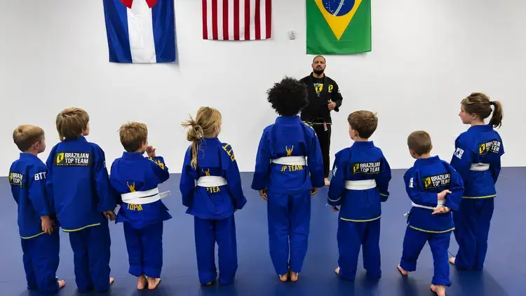 Children in blue martial arts uniforms stand in line facing their instructor in a gym.