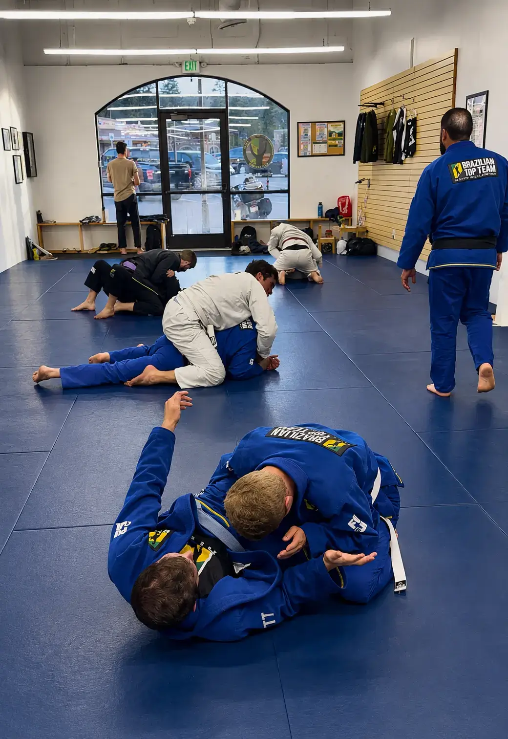 Martial artists in gis practice Brazilian Jiu-Jitsu grappling on blue mats in a gym.